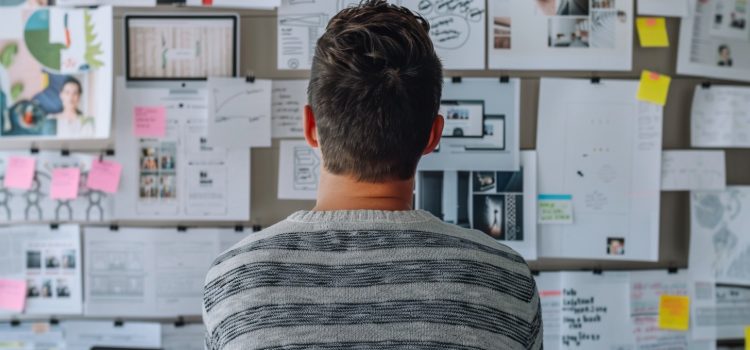 A man looking at a wall of papers and notes using outcome-based planning.