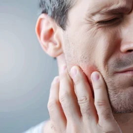 A man with jaw problems who is touching his jaw with a look of pain on his face