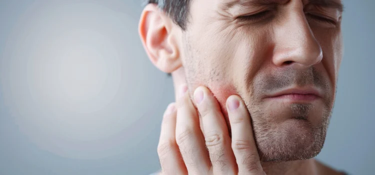 A man with jaw problems who is touching his jaw with a look of pain on his face