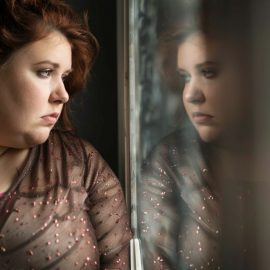 a sad overweight woman looking in a mirror raises the question, Why is body shaming bad?