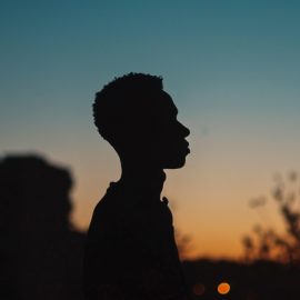A silhouette of a man outside thinking about masculinity against a sunset.