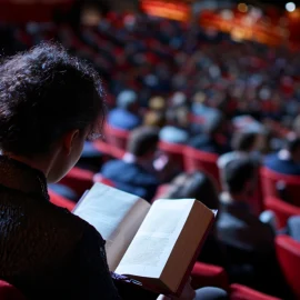 A woman reading a book while sitting in the audience of a theater