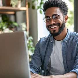 a smiling bearded man with eyeglasses engaging in online content creation at a computer in a room with lots of plants