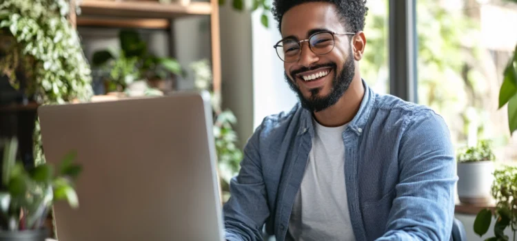 a smiling bearded man with eyeglasses engaging in online content creation at a computer in a room with lots of plants