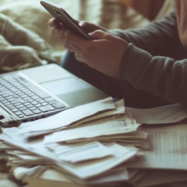 A person texting with their laptop open and papers next to them, showing one of the reasons why we procrastinate