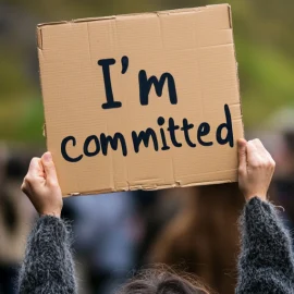 a woman holding up a sign that says "I'm committed" illustrates how to influence change that lasts