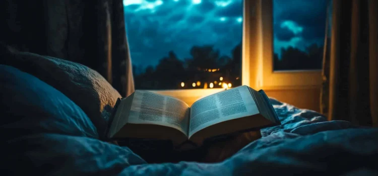 An open book on a bed looking out a window at night