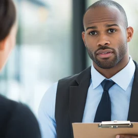 A manager holding a clipboard that has what to look for in an employee on it, while interviewing a prospective employee