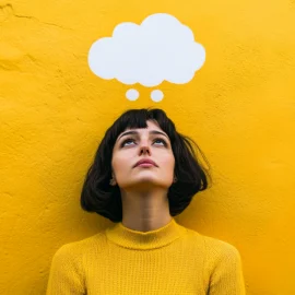 A woman keeping an open mind in front of a yellow wall with an empty thought bubble