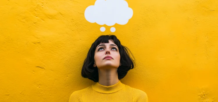 A woman keeping an open mind in front of a yellow wall with an empty thought bubble