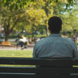 A man sitting on a park bench watching people because mindfulness and art are connected