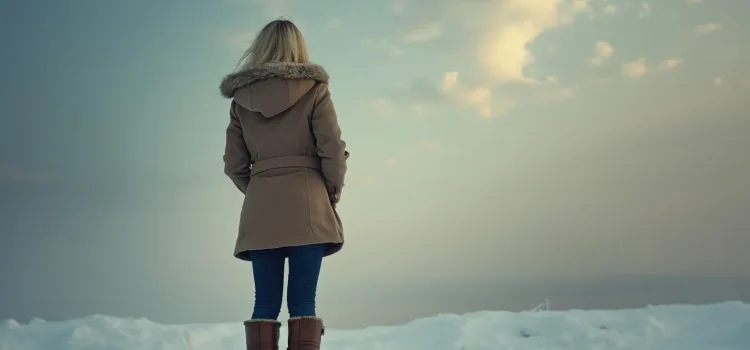 A woman seen from the back standing in show and looking into the clouds illustrates how to overcome toxic shame