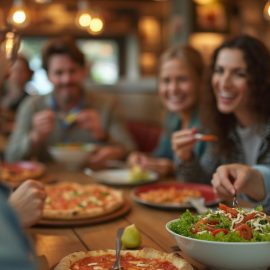 A smiling woman eating a salad in a restaurant while other people are eating pizza illustrates willpower training