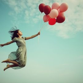 A woman floating in the air and holding helium balloons by the strings illustrates how to raise your self-esteem