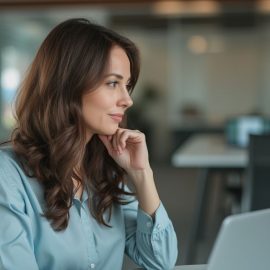 A woman with a light blue shirt and long brown hair sitting at a desk in an office contemplates career advice