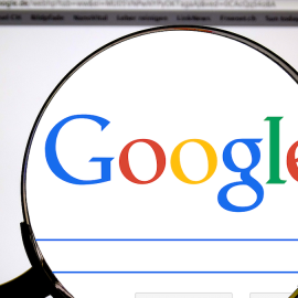 A magnifying glass magnifying "Google" on the Google search homepage illustrates the Google antitrust ruling