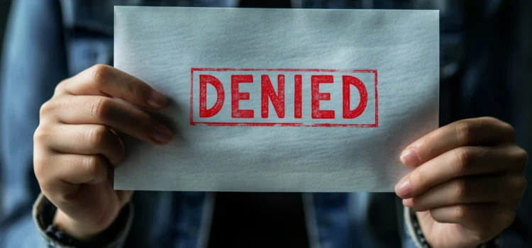 Hands holding an envelope that has the word "denied" stamped on it with red ink because of the health insurance crisis in the US