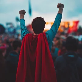 A man dressed as Superman with a red cape doing a superhero pose in a crowd, showing the importance of power