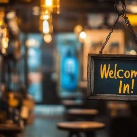 A sign that says "Welcome In!" on a window peaking into the retail environment of a store