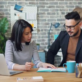 A man and woman in an office, sitting at a desk together, participating in creative collaboration