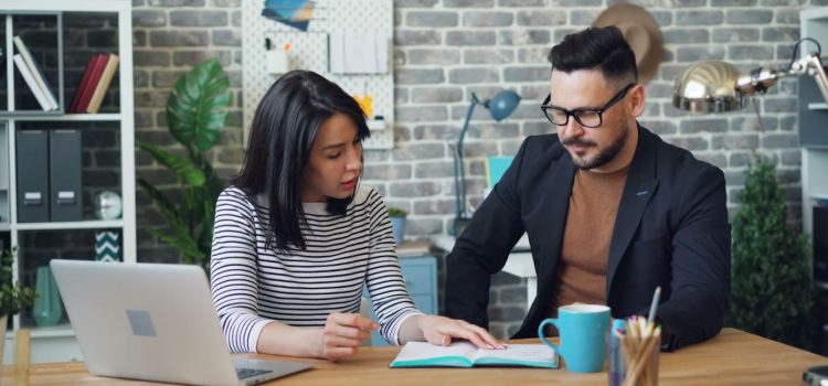 A man and woman in an office, sitting at a desk together, participating in creative collaboration